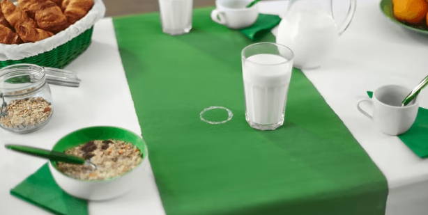 Glasses of milk and bowls on a tablecloth. A ring of milk stains the tablecloth.