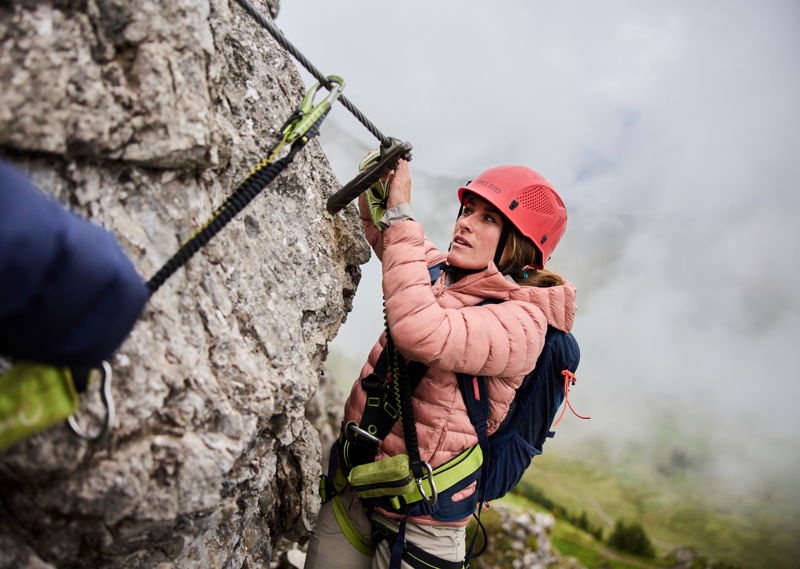 Frau am Klettersteig im Kleinwalsertal nahe Mittelberg mit Sicherung und Helm.