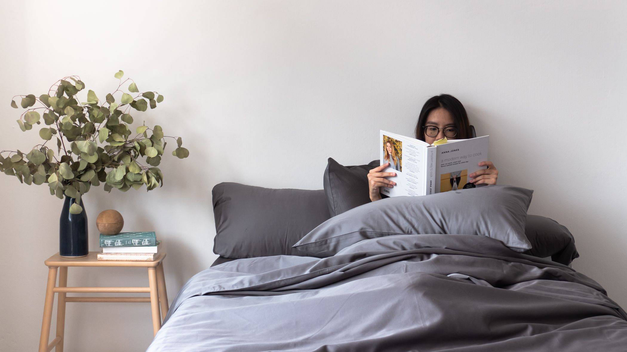 Girl reading a book in bed with Weavve's TENCEL Lyocell grey bed sheets