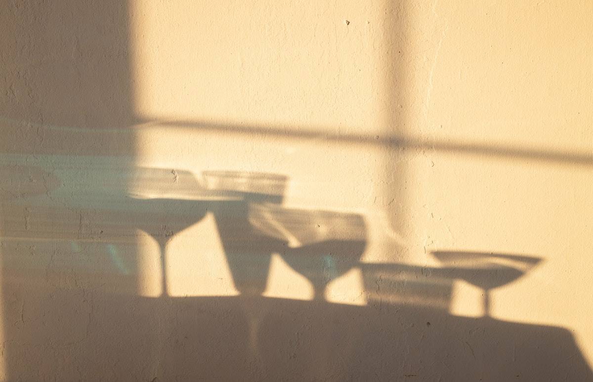 Shadow of various wine glasses on a blank wall .