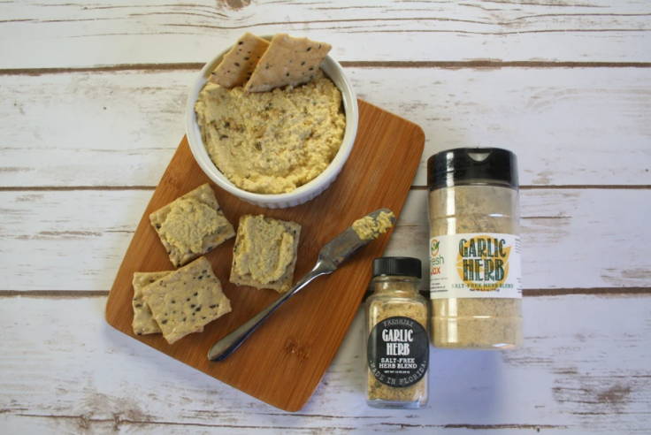 Plant based garlic herb spread with crackers next to two bottles of FreshJax garlic herb blend. 