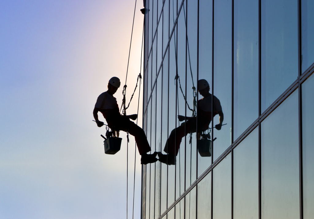 Male worker attached to a rope with specialist cleaning tools to maintain a tall building at height.