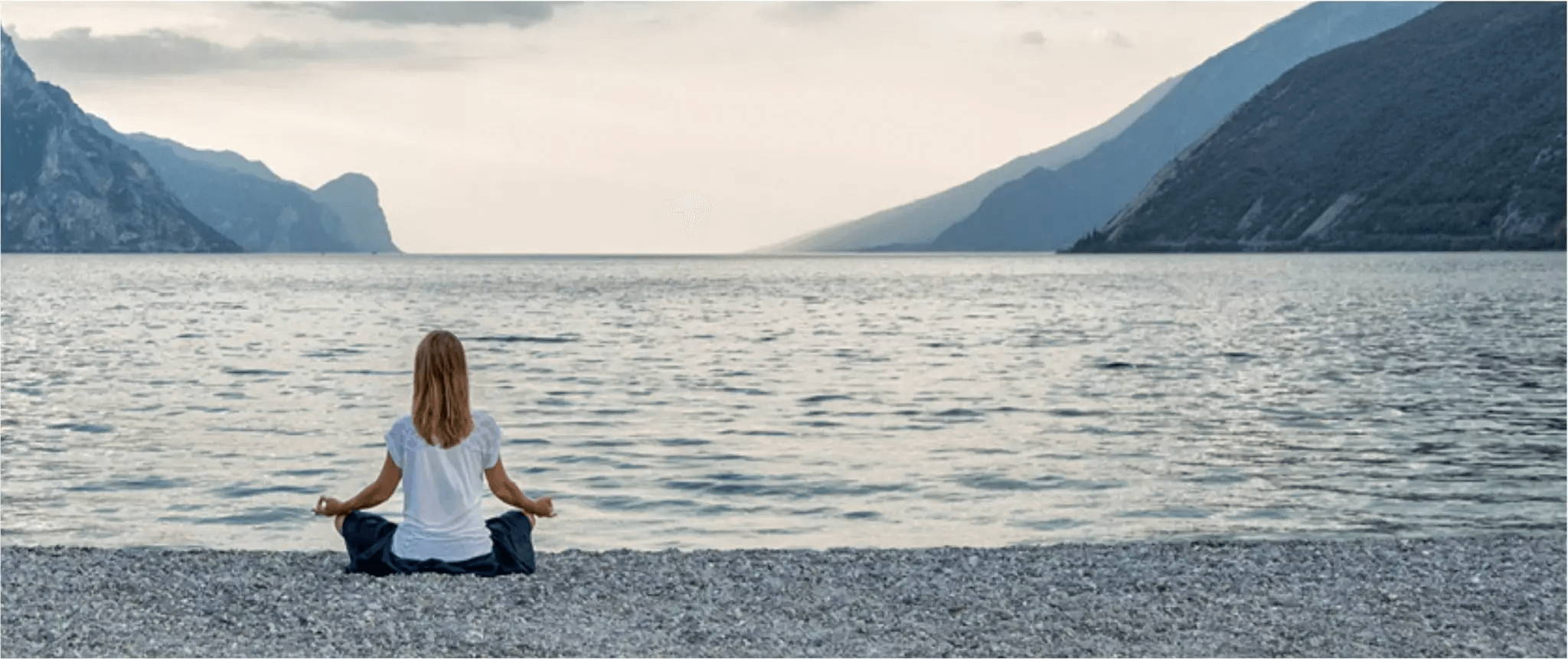 blonde haired woman, in a white shirt meditating on the edge of the water