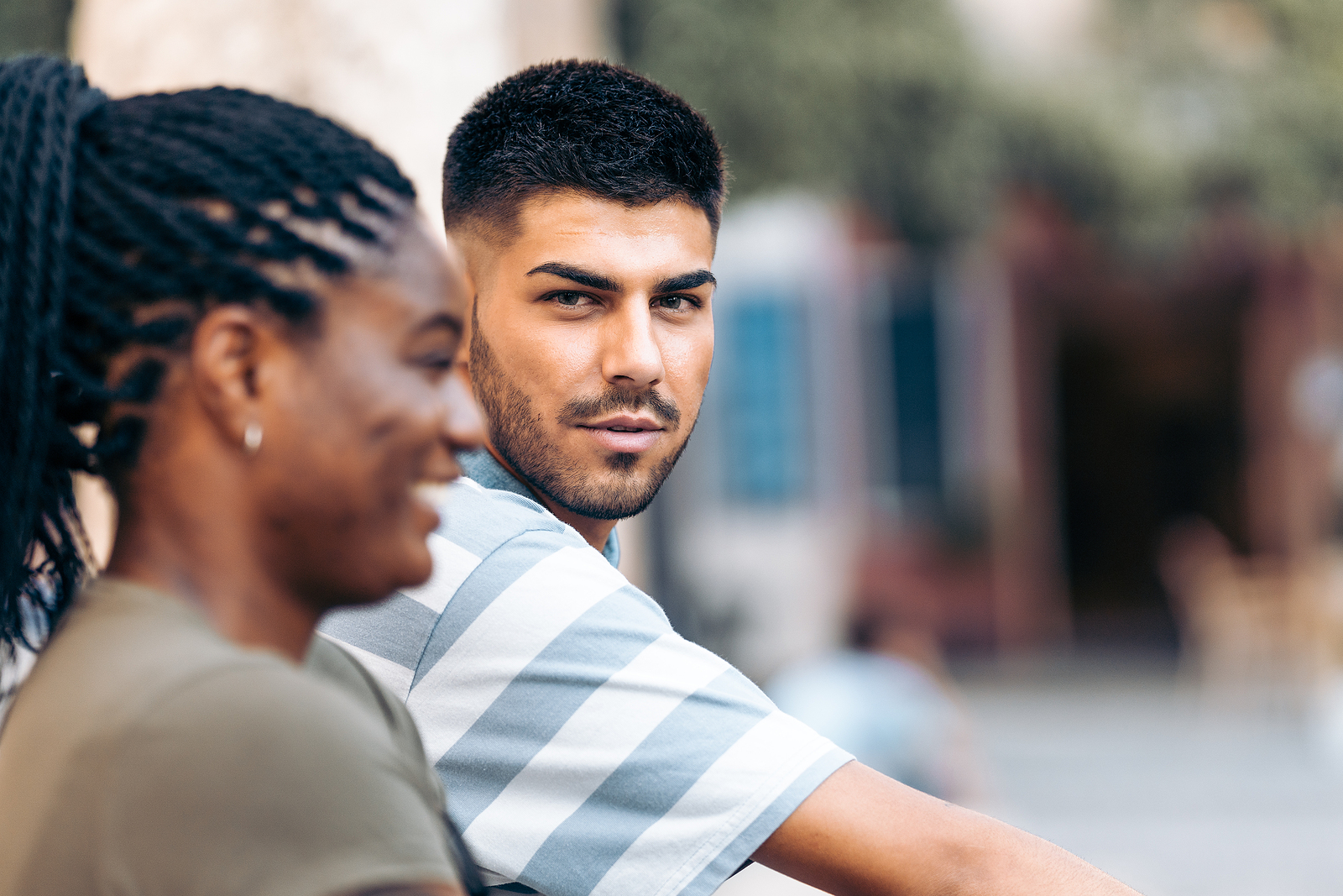 A multi ethnic man looks over to his black friend on his side. She is laughing.