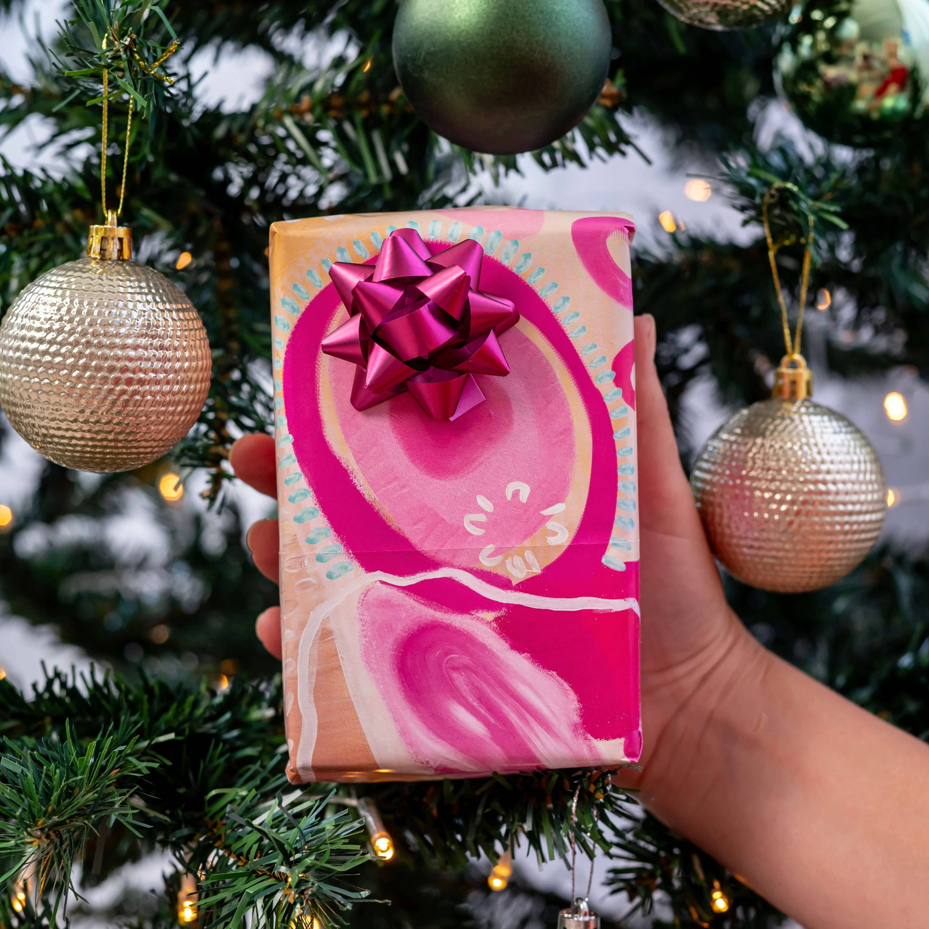 Gift in pink wrapping of Indigenous artwork in front of Christmas tree