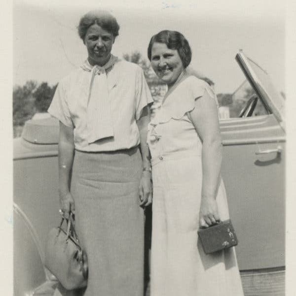 Eleanor and Lorena standing close in front of a car. They are both smiling at the camera, Lorena more serious.