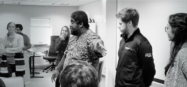 d'un homme barbu vêtu d'une chemise imprimée s'adressant avec animation à un groupe d'employés de Mysa à l'air engagé, dans un bureau moderne