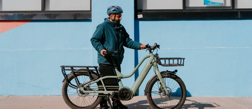 a wman standing next to a green Momentum PakYak E+ electric cargo bike