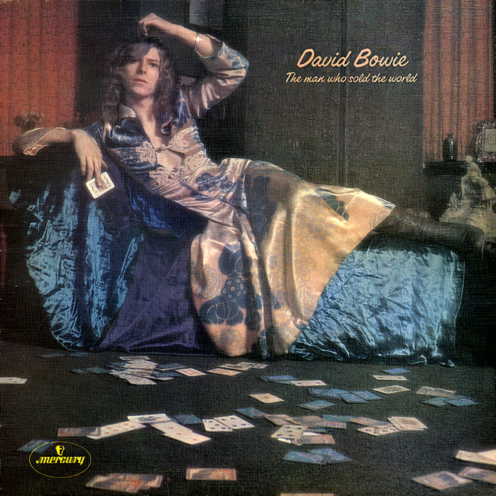 Album cover for the man who sold the world. Bowie is laying on a long seat wearing a dress holding a card in hand.