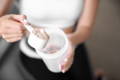 woman pouring one scoop of collagen powder into a cup