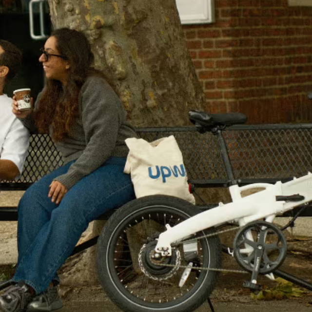 a woman sitting on a park bench next to a lectric electic bike