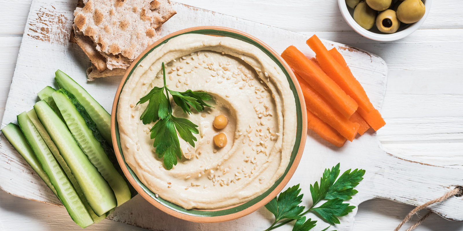A bowl of hummus with veggies, olives and pita bread