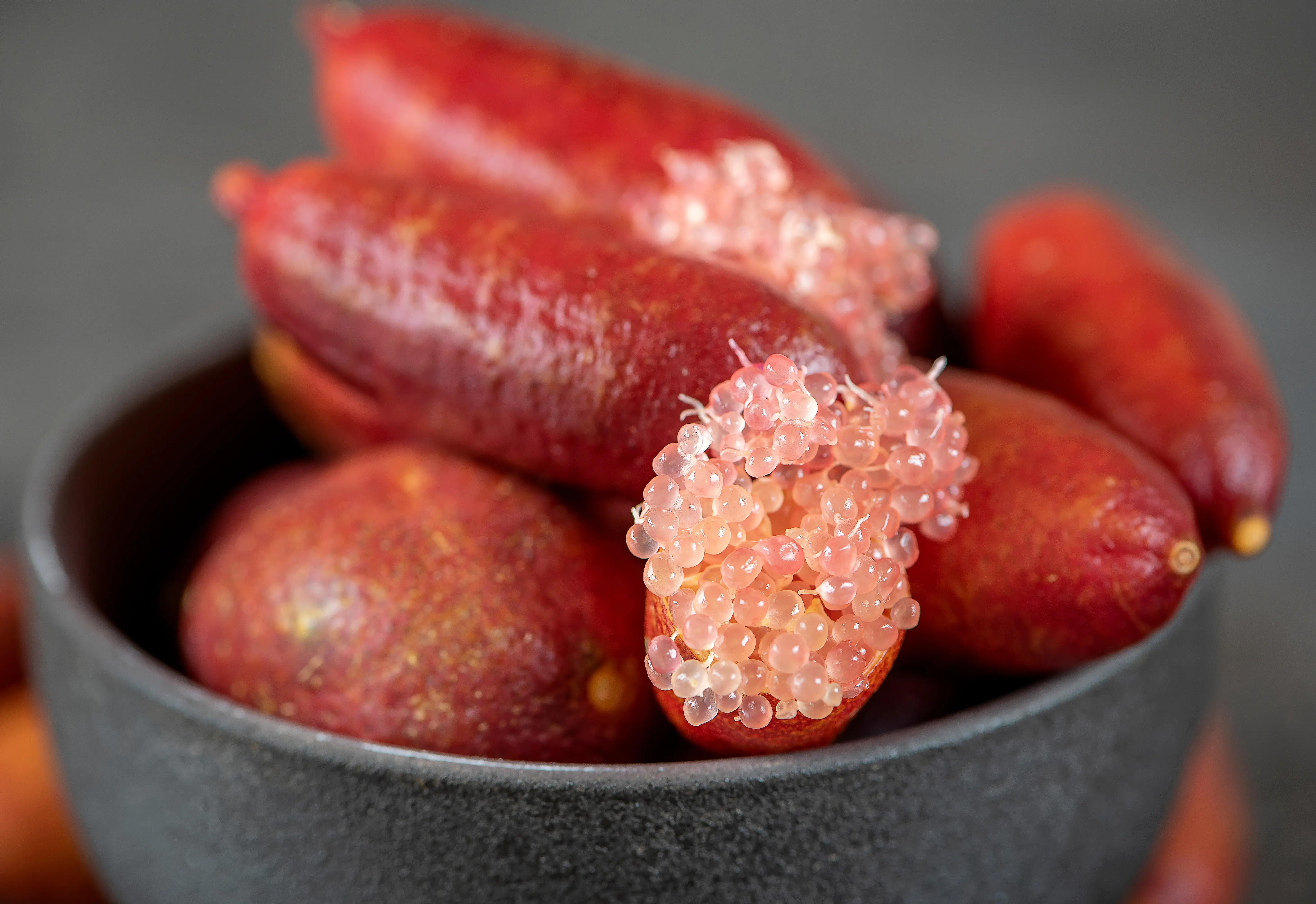 An image displaying Fingerlime fruit - the fruit depicted is red and oblong, whilst the insides look much like transparent caviar.