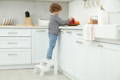 Toddler on a step stool in a kitchen.