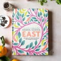 A book titled 'East' by Meera Sodha has colorful tree branches wrapping the cover of the book 