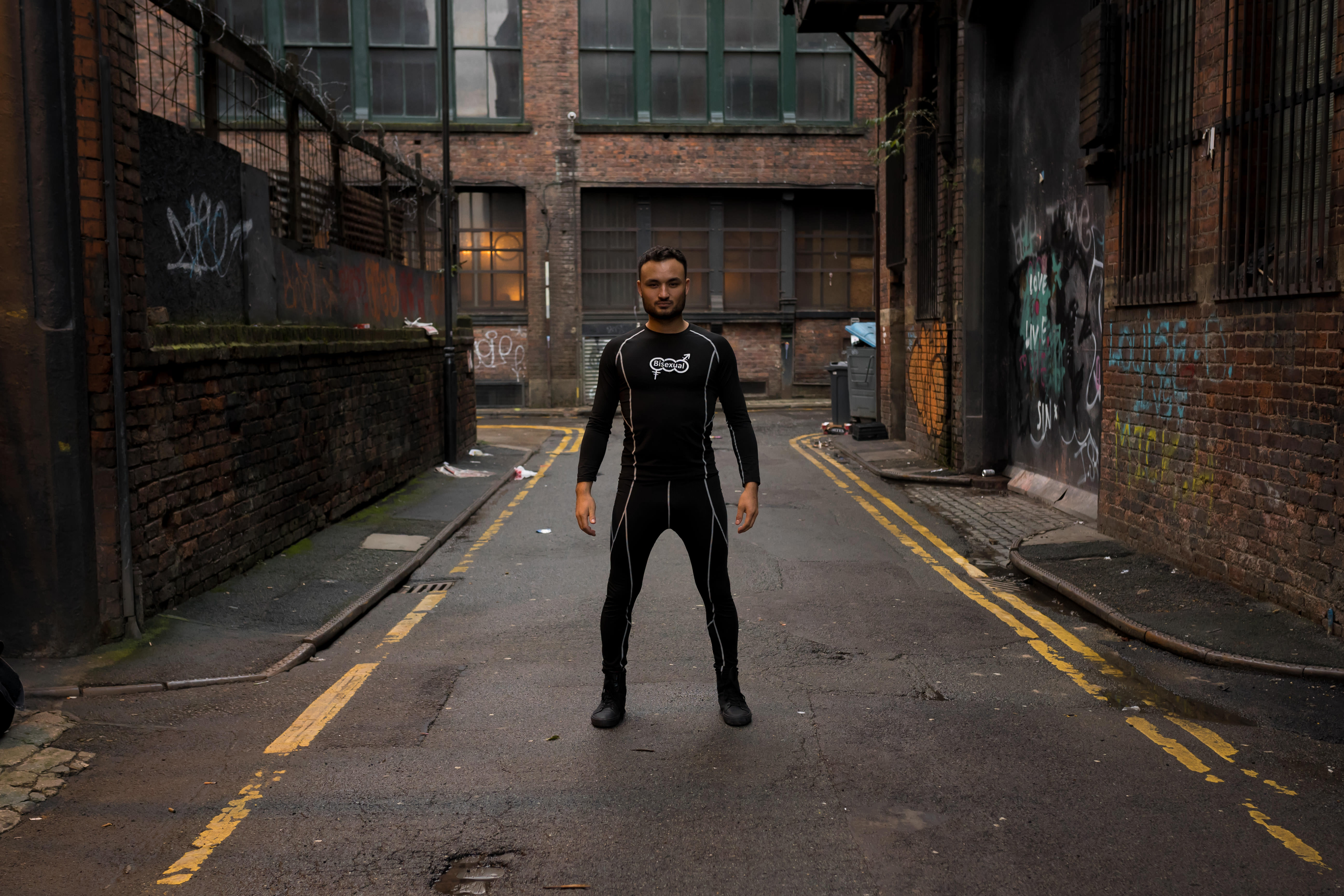 A model photograph of Lewis Oakley standing confidently in the middle of a street wearing dark clothing.