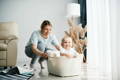 Toddler in a plastic basket pushed by his mom across the room.