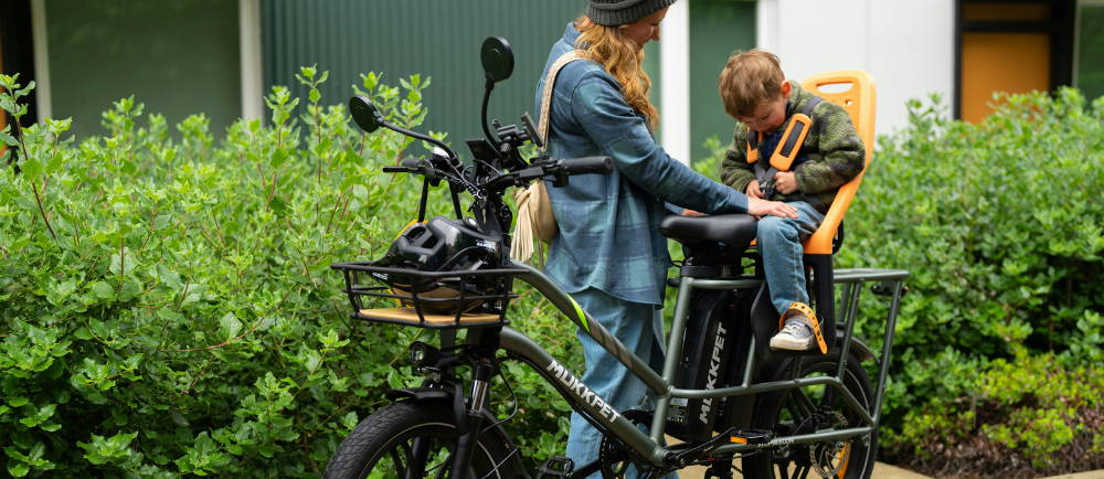 a woman strapping her kid in the back of her mukkpet electric cargo bike