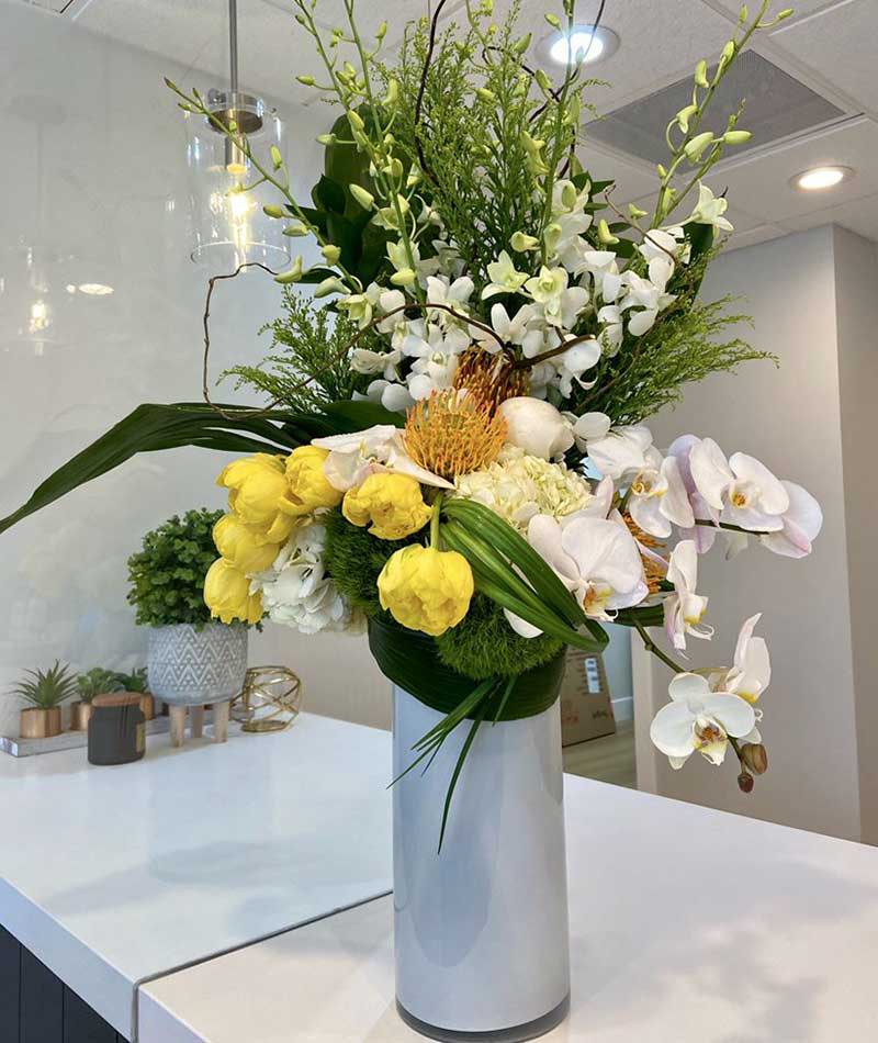 Arrangement of white, green and yellow flowers in a white vase placed on a table