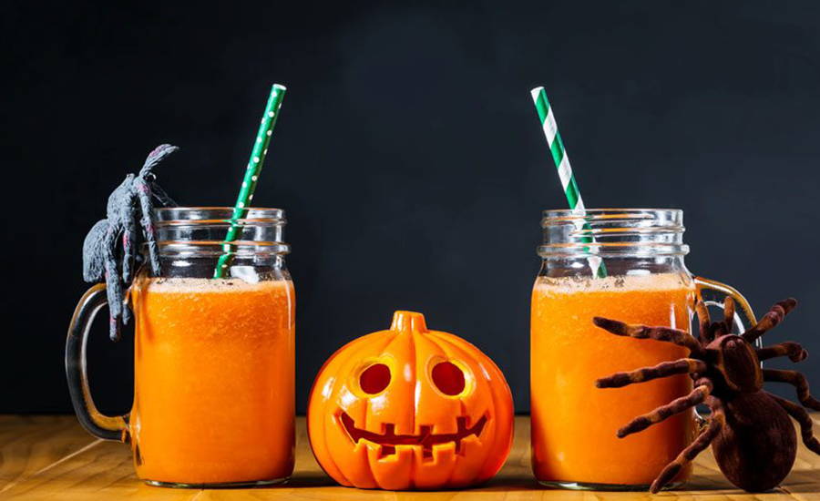 Orange drinks in mason jars with a pumpkin and spider decoration