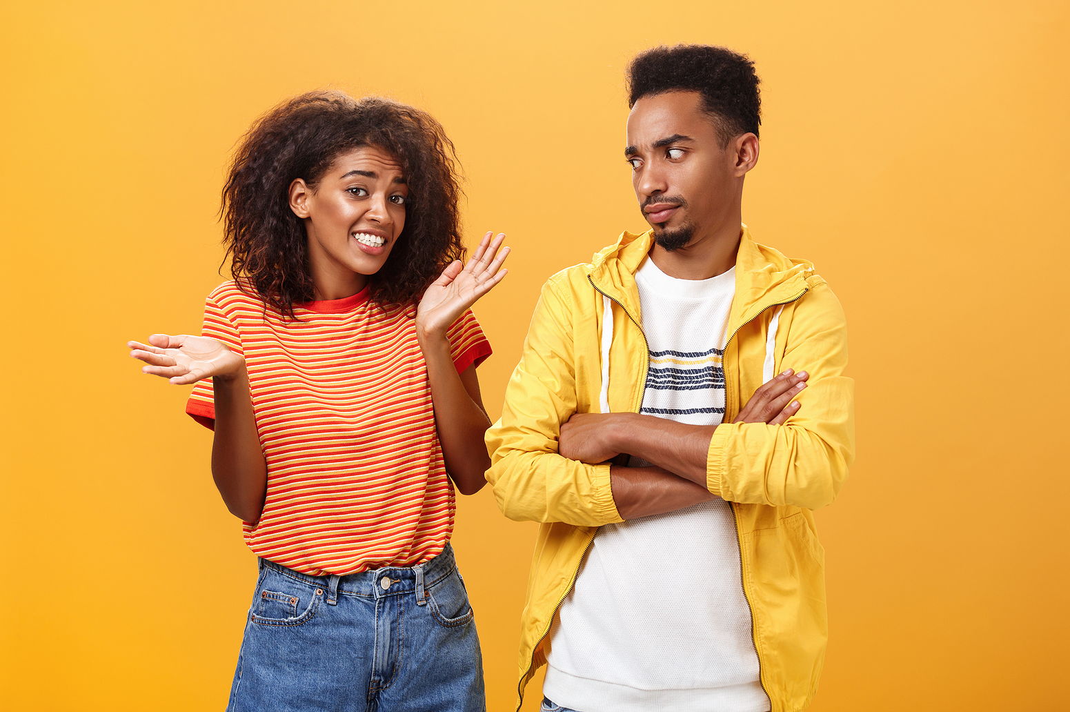 A black man and woman stand next to eachother. The girl has a nervous expression holding her hands up giving up.