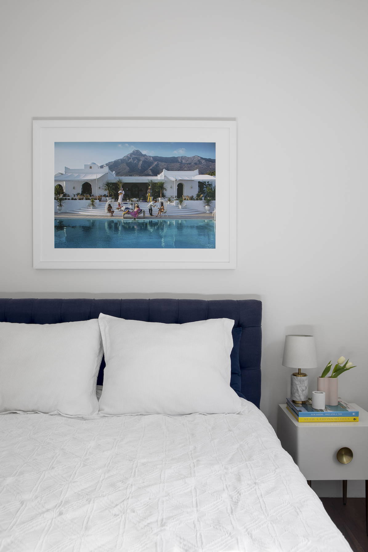 A poolside photograph by Slim Aarons, framed in white in a pretty bedroom setting