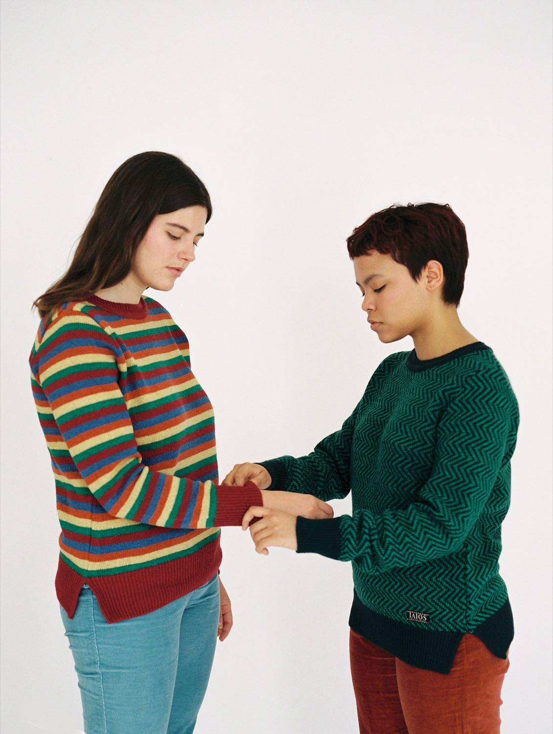 Una noia arregla la màniga del jersei a una altra. Ambdues porten jerseis iaios