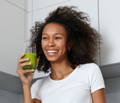 a woman standing in her kitchen drinking a glass of wheat grass juice with a smile on her face