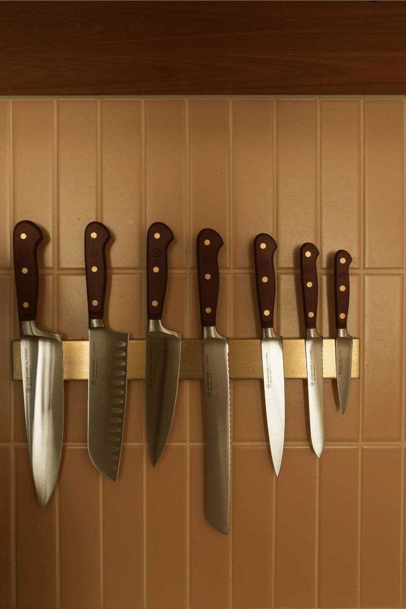 Seven WÜSTHOF Classic Colour knives on a brass magnetic knife rack above a kitchen bench