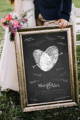 bride and groom holding black and white chalkboard fingerprint sign with wedding guest signatures