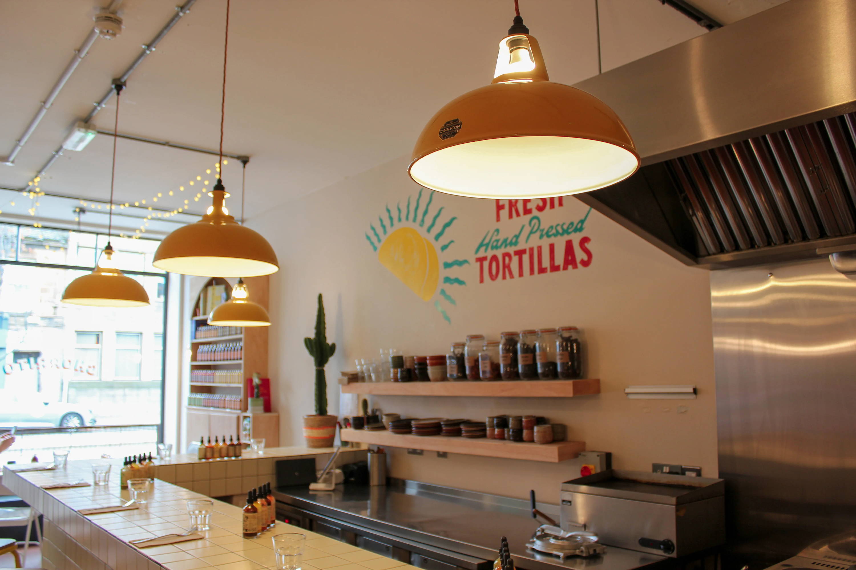 Four Large Coolicon Pendant Lampshades hanging over a tiled corner bar in a small mexican-inspired Cantina Resturaunt.