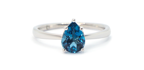 Gold ring with a drop-shaped blue topaz is set on 5 claws protecting the tip of the stone.