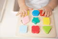 A colorful wooden Montessori puzzle toy and its pieces are sorted by little toddler hands. 