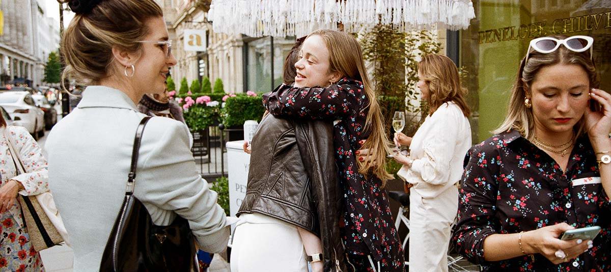 Amelia Windsor hugs her friend at the YOLKE x Penelope Chilvers Launch Party. Amelia Windsor wears YOLKE's Blossom Print Day Suit.