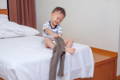 Asian toddler sitting on a bed and putting his pants on. 