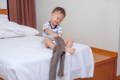 Asian toddler sitting on a bed and putting his pants on.
