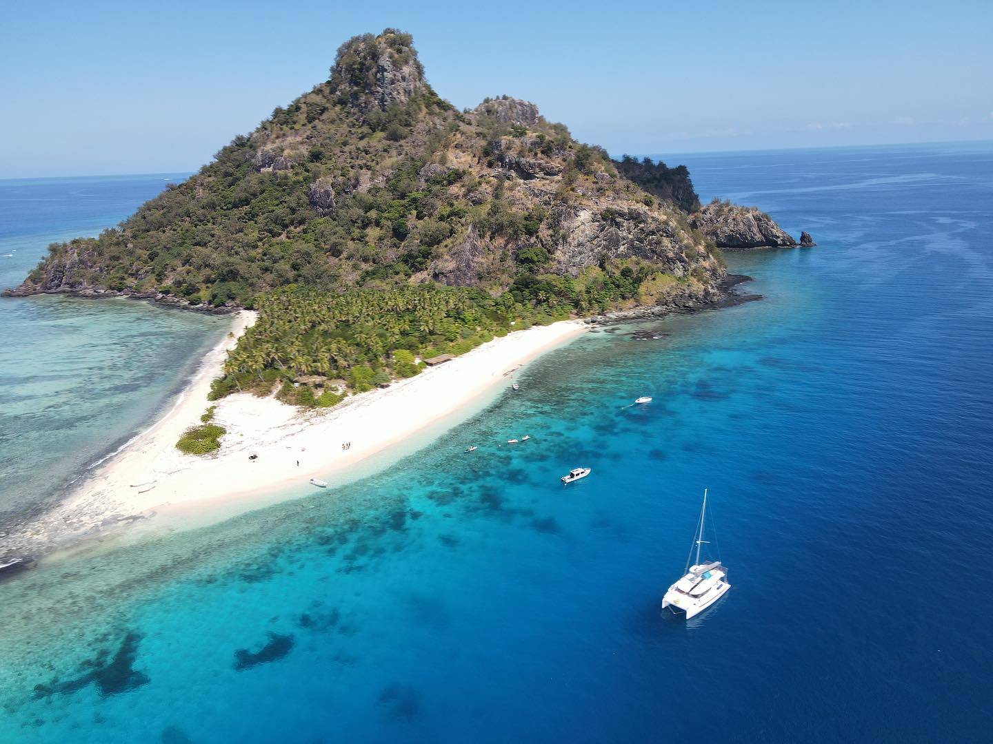 Some boats near a remote island in the Pacific Ocean, small group on beach with dinghy