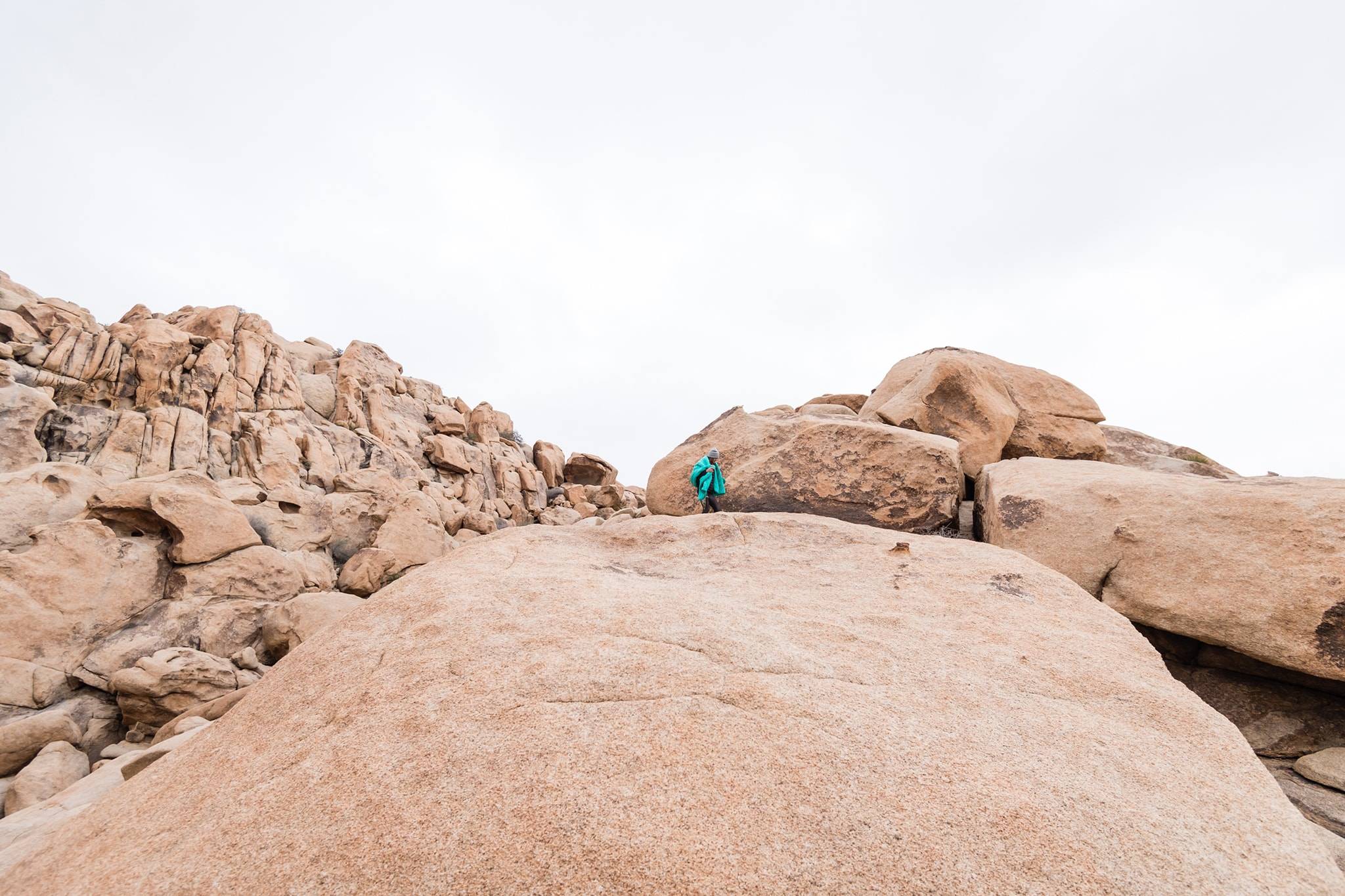 Man standing on a large rock in Joshua Tree National Park with a green Rumpl blanket