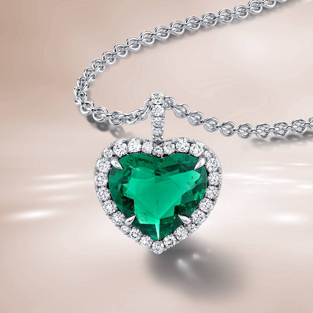 Heart shaped emerald pendant necklace with diamond halo on a brown background.