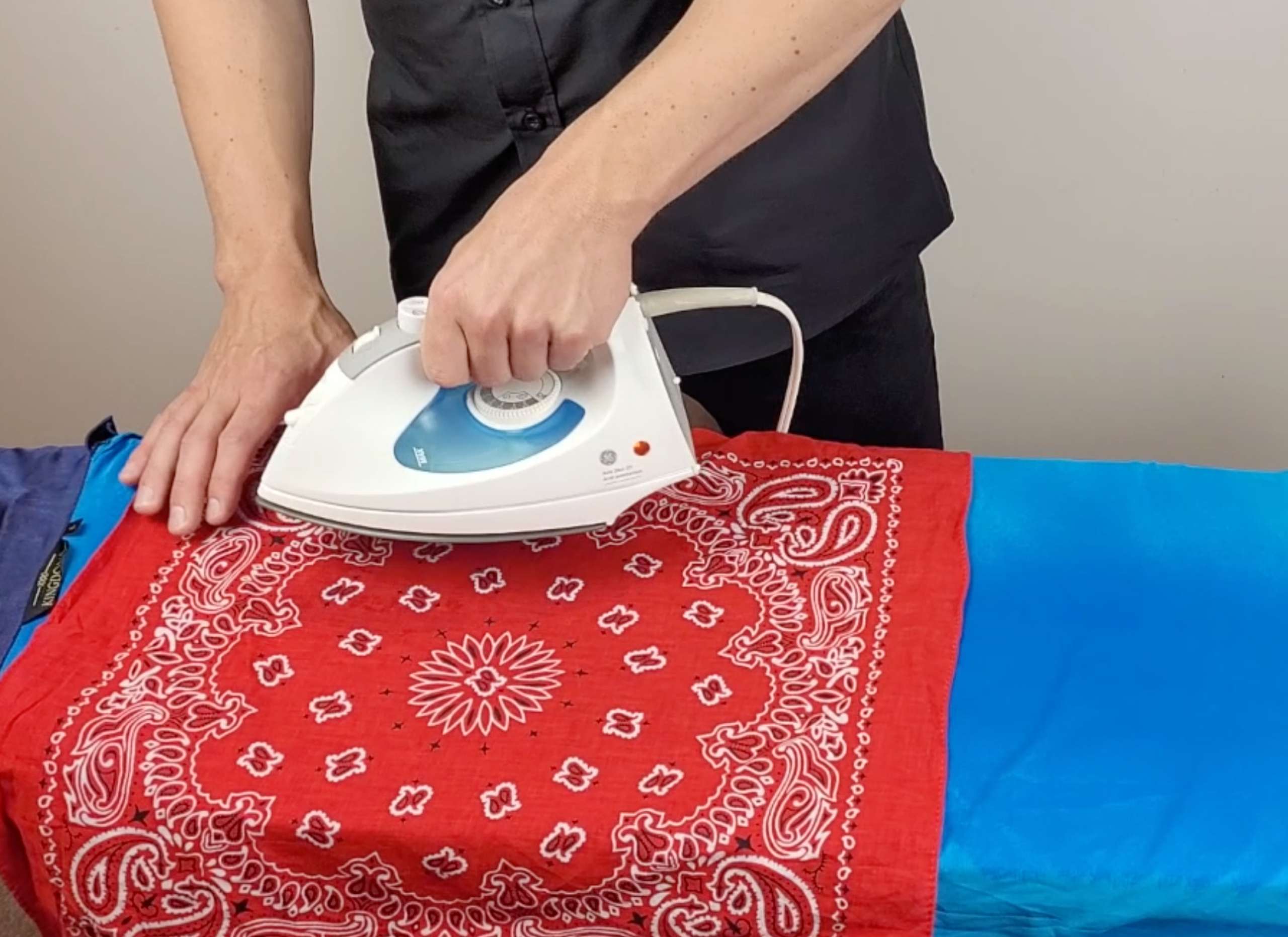 a photo of a man ironing blue silk pajamas on an ironing board