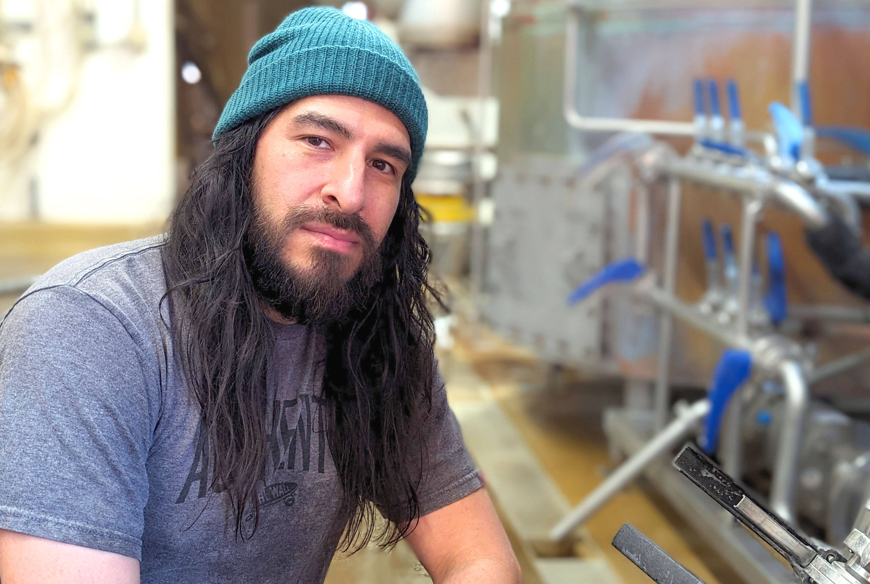 Man in a beanie and t-shirt next to brewing vats