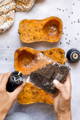 3 halves of butternut squash sit beneath a set of hands refilling a pepper grinder from a clear plastic bag full of peppercorns