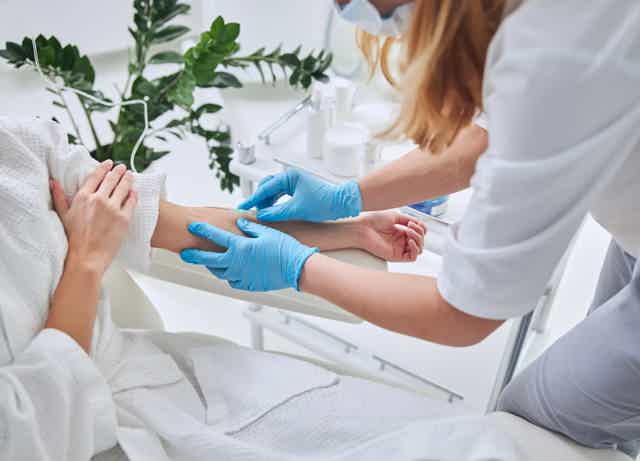 Medical professional applying gloves and injecting vaccine in patient’s upper arm in clinic, with supplies on counter