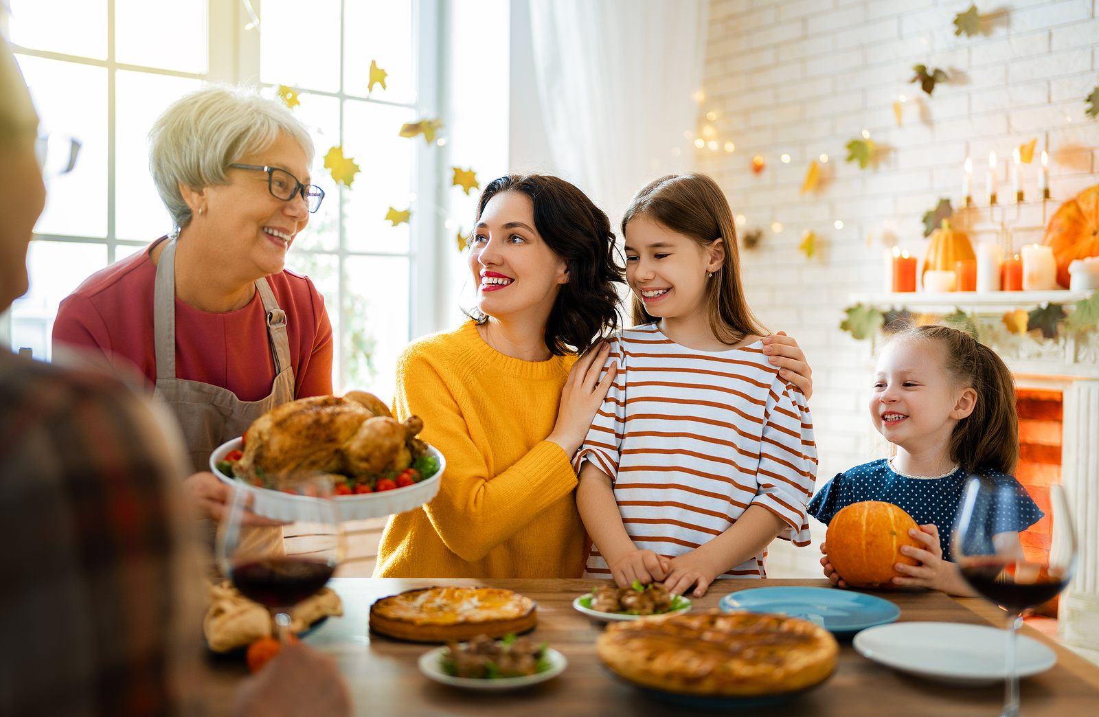 A mom holds her daughter as she cuts a pie. They all laugh and look at the grandma while at the dinner table.