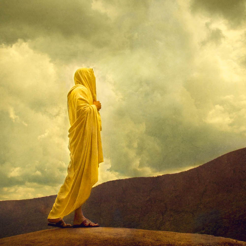 Jesus standing on a hill looking up toward Heaven. He wars a yellow robe.