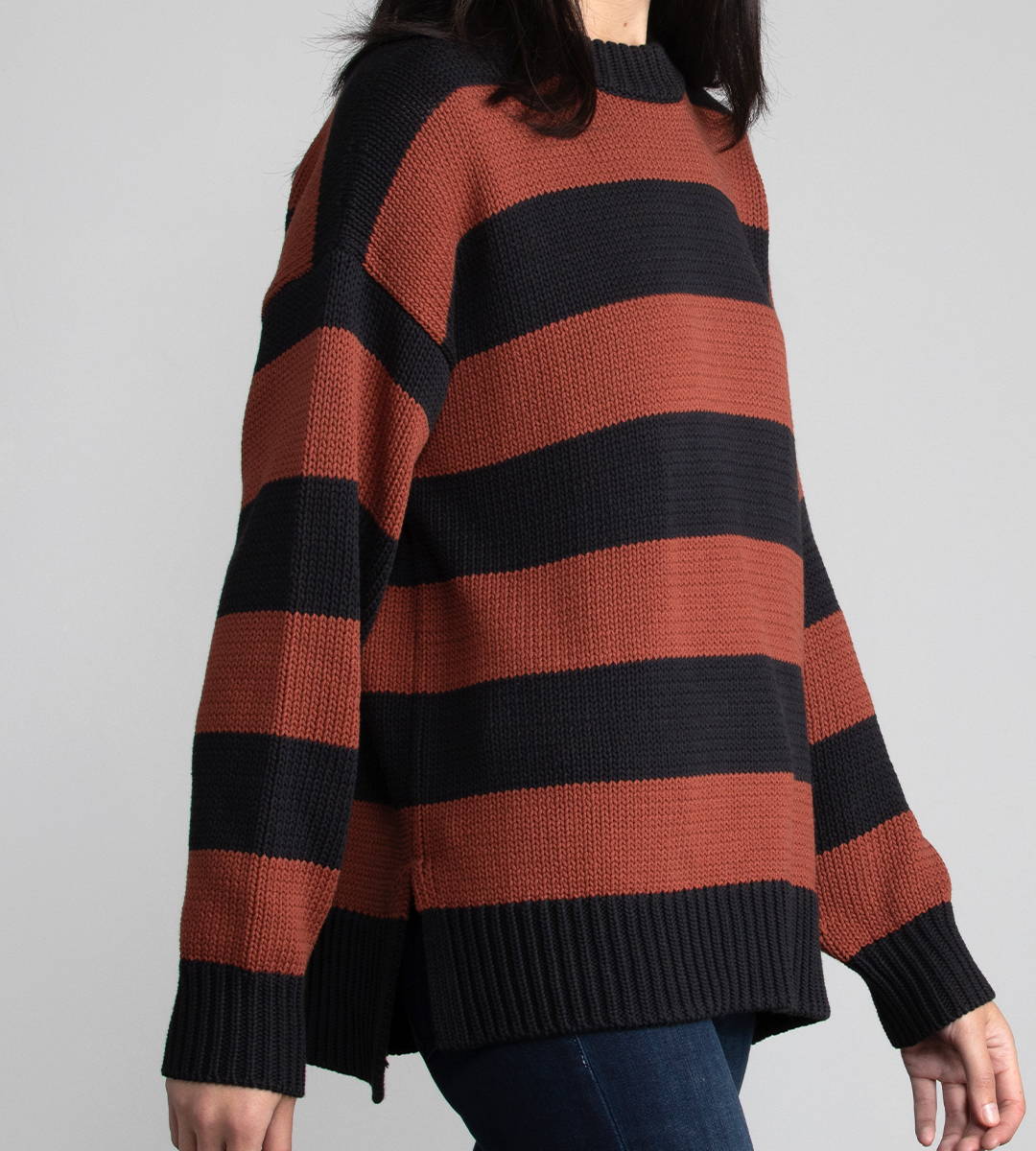 Close up image of a woman walking. She is wearing a black and red striped crew neck sweater.