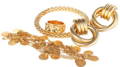 Gold Jewelry Collection with Earrings, Rings, and Coin Bracelet An assortment of yellow gold jewelry including a wide textured ring, ribbed hoop earrings, a mesh bangle, and a coin charm bracelet against a plain white background