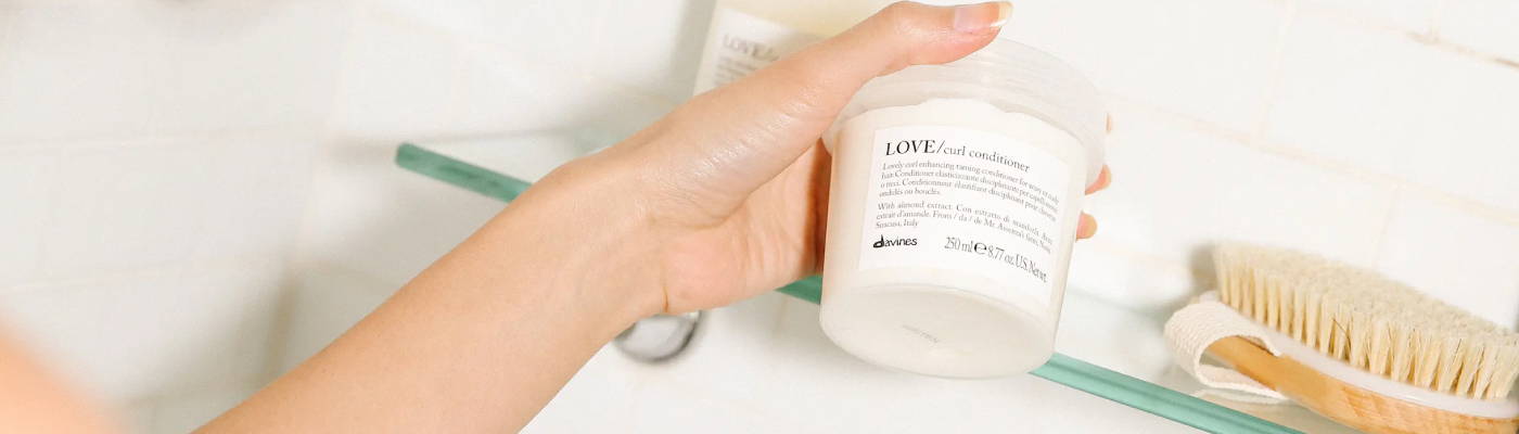 hand in the shower reaching for Davines' LOVE/ Curl Conditioner on the shelf