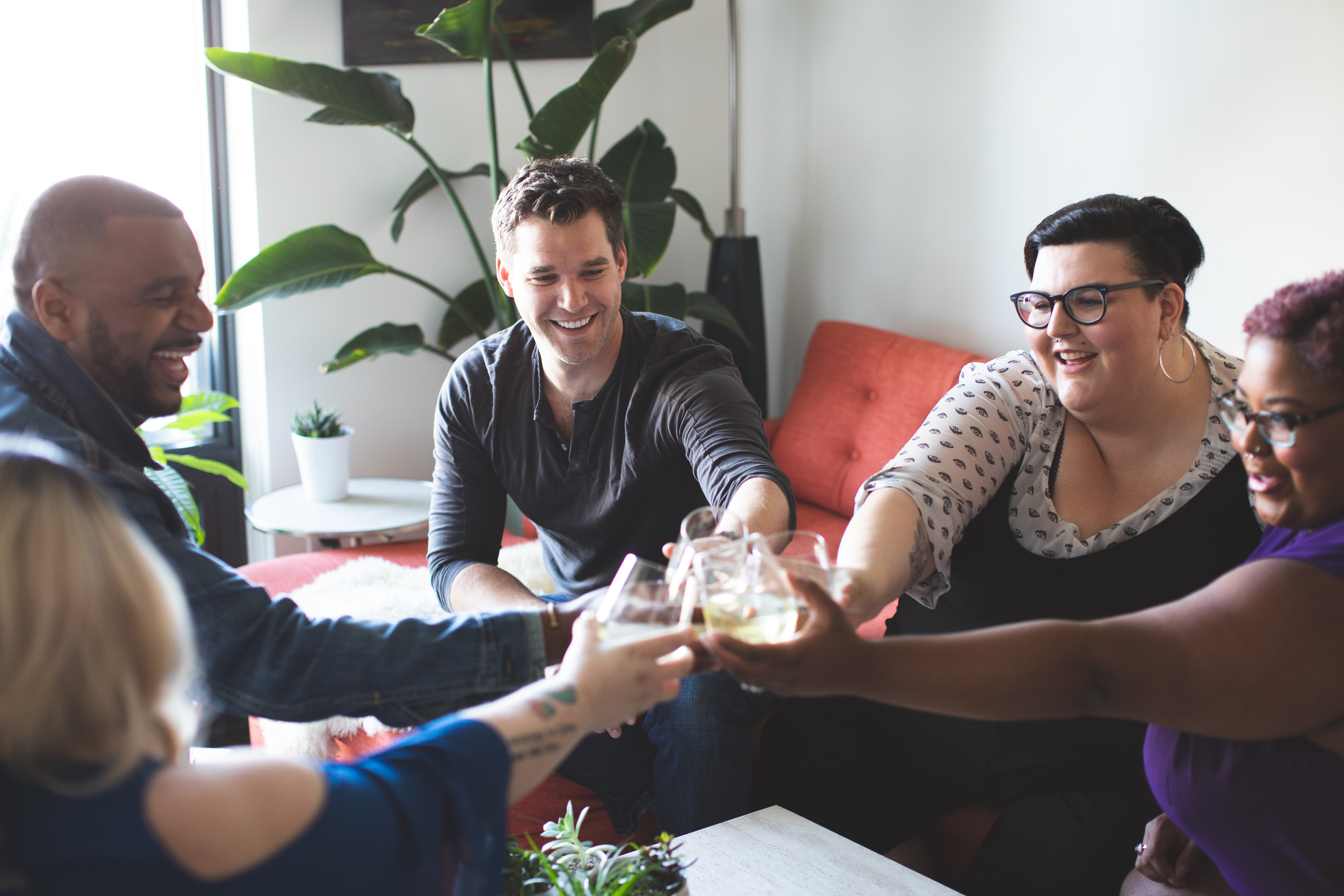 An inclusive group of multi ethnic men and women sitting together doing a cheers with glasses.