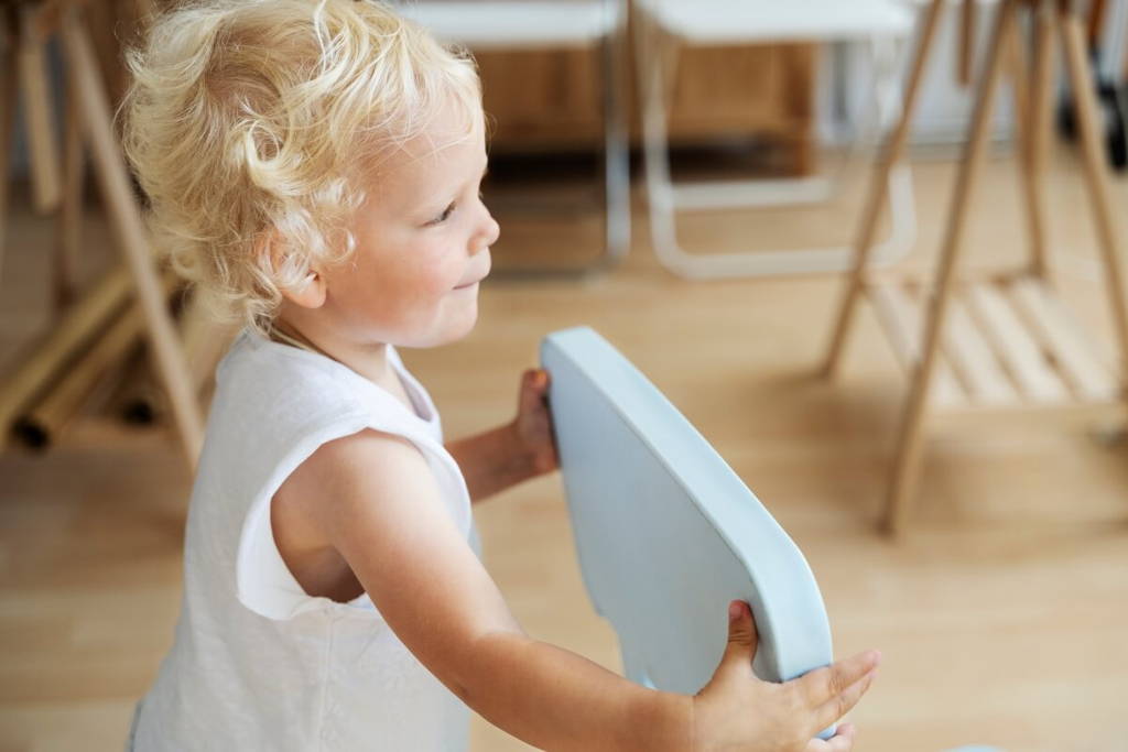 Blonde toddler holding moving a chair.